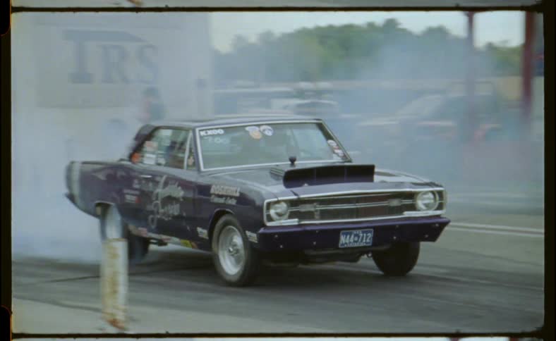 People stand on a track as smoke billows from a race car as it drives off
