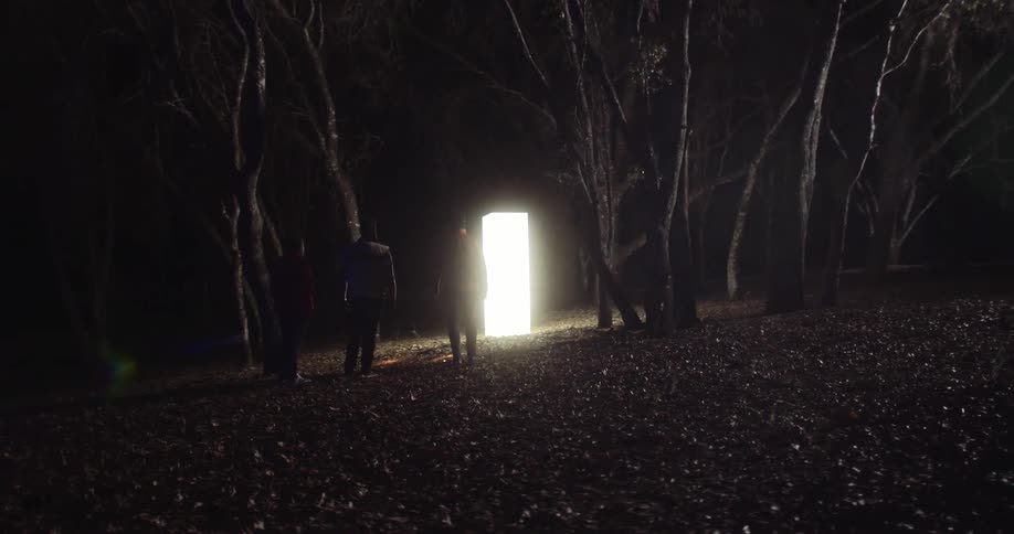 A group of men stand around a monolith glowing in a forest at night