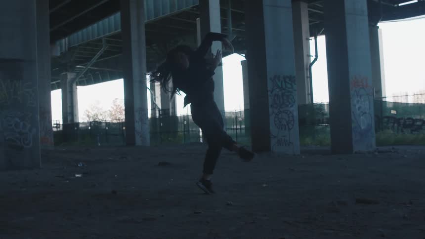 A teenage girl dances under a bridge