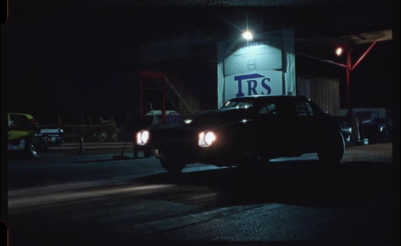 A man walks through a private parking lot past a business and a vehicle warming up at night