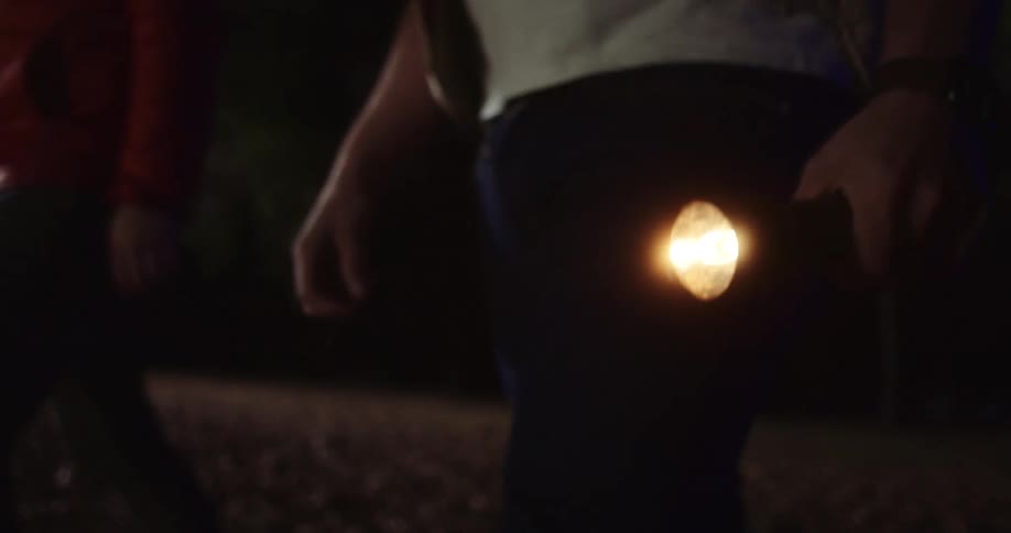 Two people walk through a dark area at night with flashlights