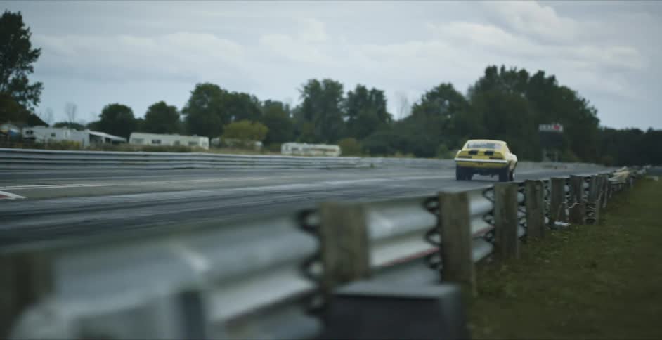 A vehicle driving on a racetrack with trees the sky and clouds in the background
