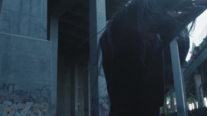 A person dancing underneath an overpass with pillars and graffiti in the background