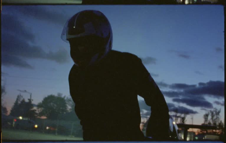 A person with a helmet going into a formula one race car with trees the sky and clouds in the background
