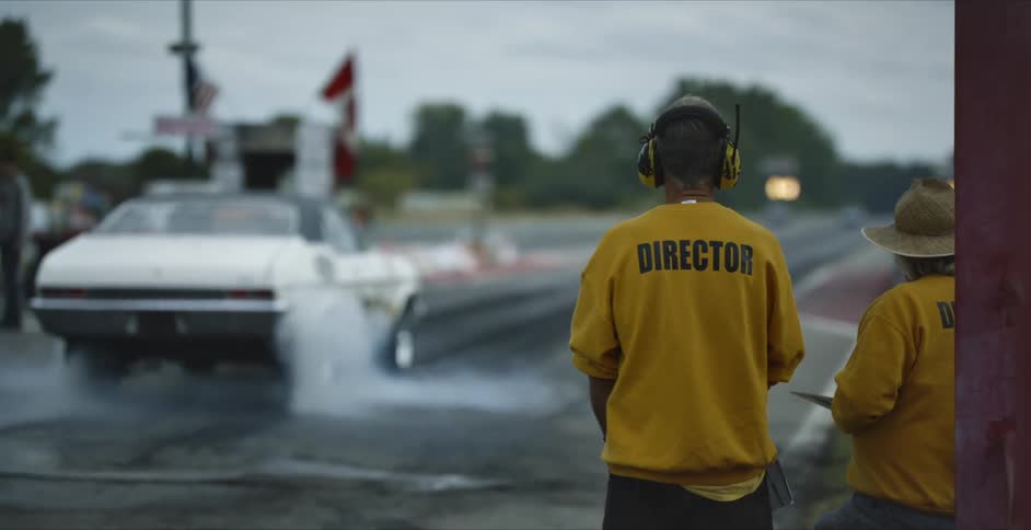 People watch as a race car spins its wheels and smoke comes off of them