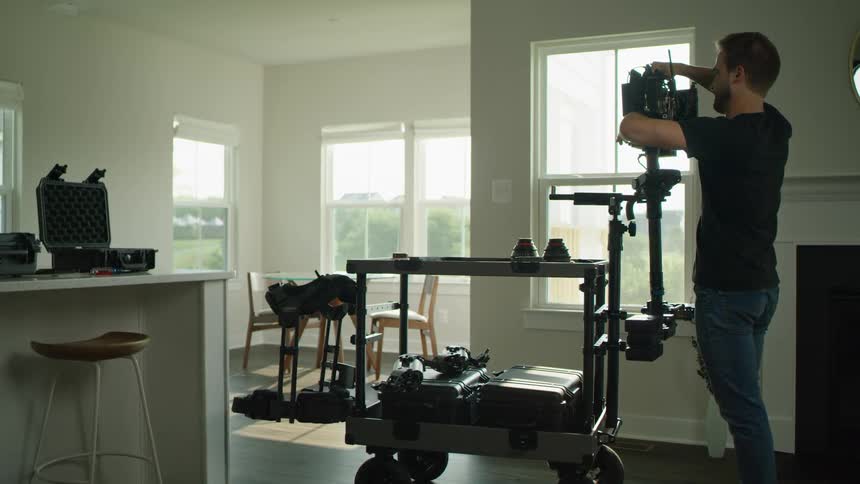 A man in a room putting a camera on a cart with a wall and window in the background