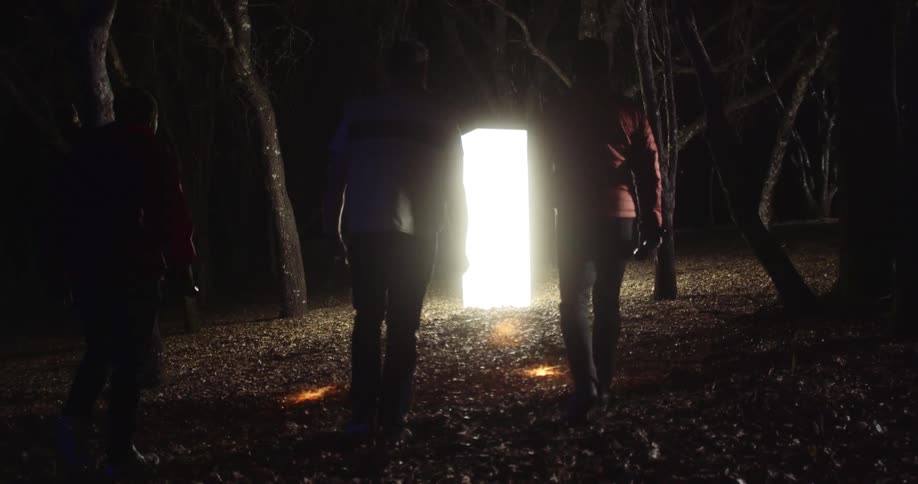 Three men with flashlights walking towards a pillar of light surrounded by trees