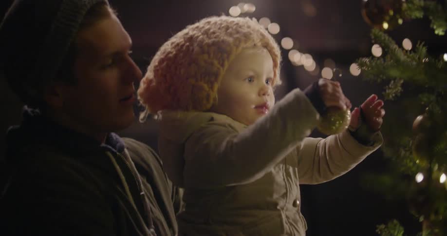 A man hands a baby a christmas ornament to hang on a tree