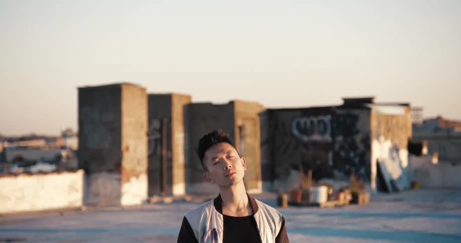 Man standing on lot with buildings in background closes his eyes as sun shines on his face