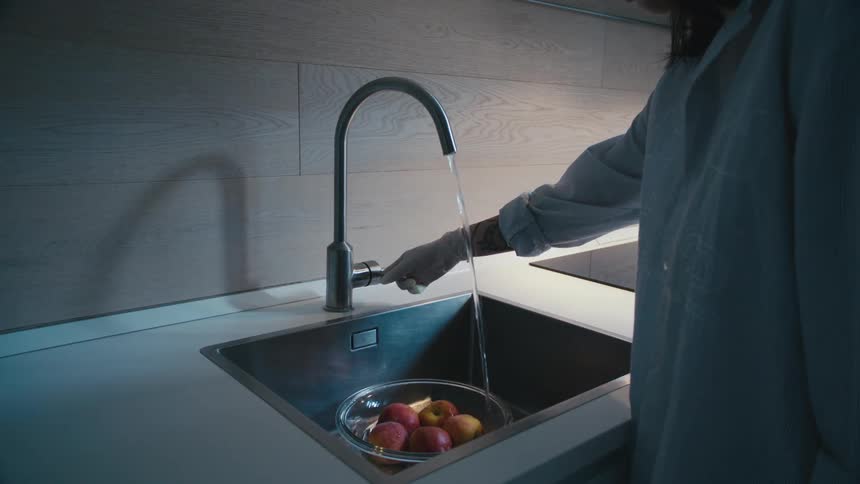 Woman wearing translucent gloves turns on faucet to rinse bowl of fruit