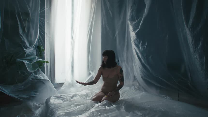 A woman in a room surrounded by plastic with a wall and window in the background