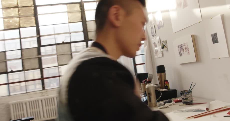 A man sits down at a desk where he begins work on a painting