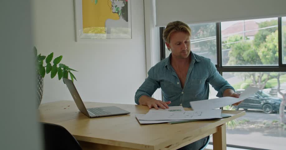 Blonde man with a blue shirt sits at table and makes a video call on laptop in the office