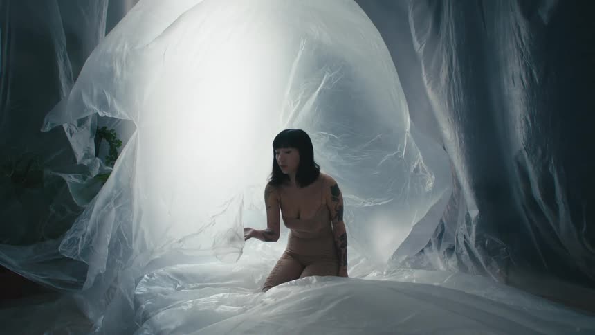 A woman in a room surrounded by plastic with a wall and a window in the background