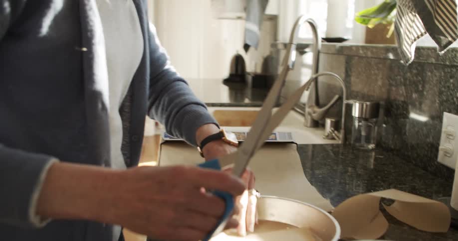 A man and a woman in a kitchen with the woman cutting wax paper with a scissors