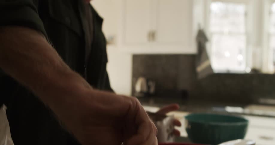 A man with glasses in a kitchen putting a scoop of chocolate powder into a strainer in a bowl