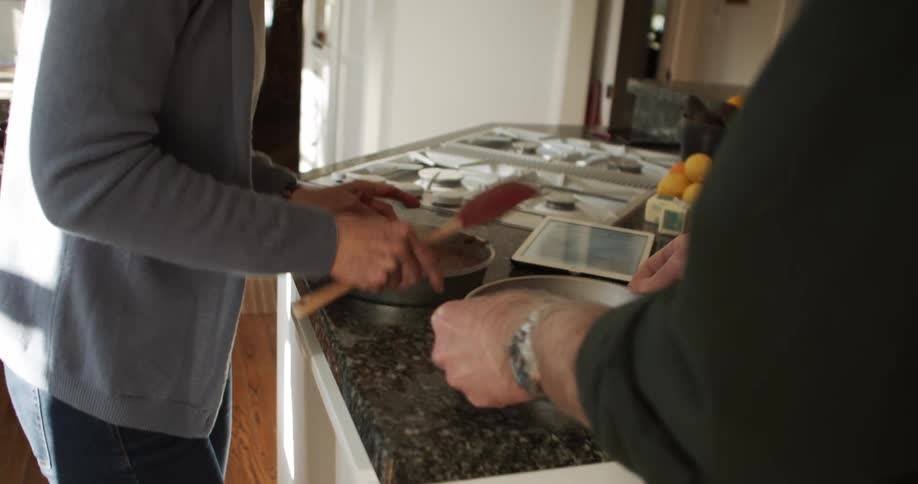 A man and woman shake pans to loosen the cake inside while standing in a home kitchen during the day