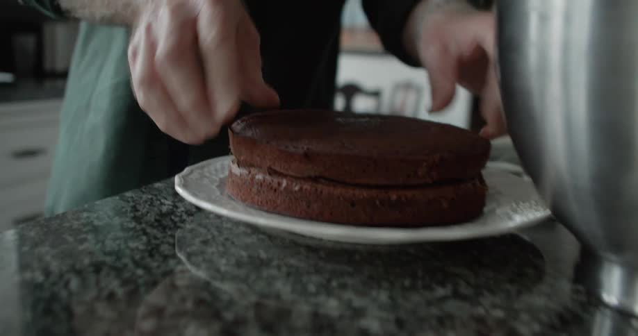 A man layers sections of chocolate cake together in her kitchen