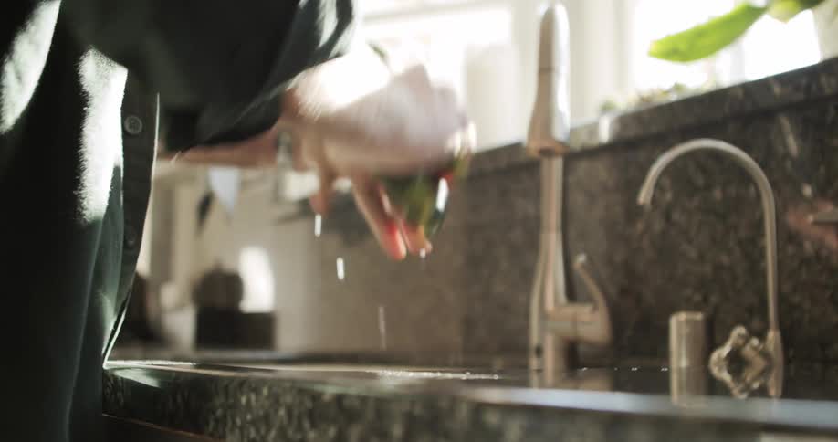 A male washes three green zucchinis under water in his kitchen sink
