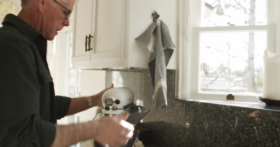 A man carries an electric mixer and places it on the kitchen countertop