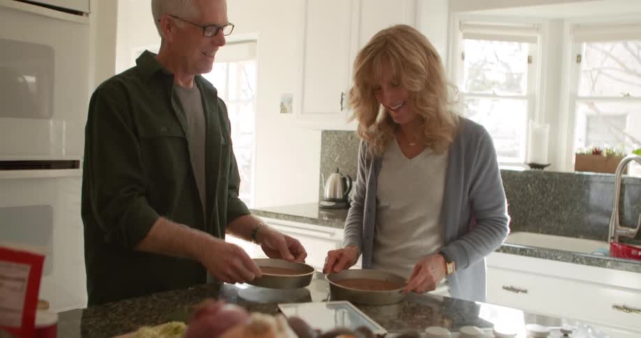 A man and his wife shake pans to remove cake in their kitchen