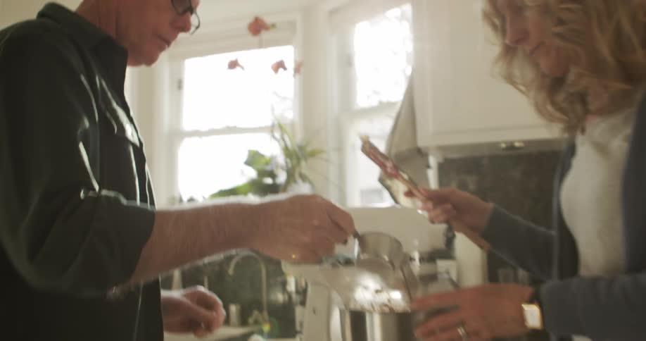 Man and woman add ingredients to standing mixer in kitchen