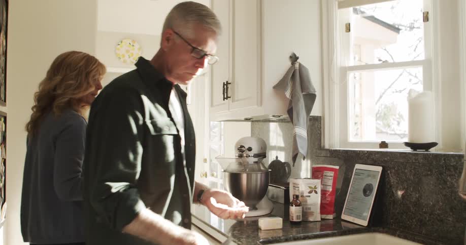 Woman joins husband near standalone mixer as he holds paper wrap and butter knife