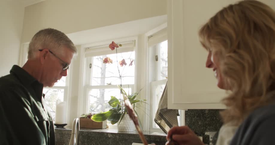 Man wearing glasses a dark shirt and blonde woman use a stand mixer and taste food in the kitchen