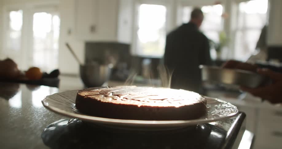 A woman walks over to a plate upon which a freshly baked cake is cooling in her kitchen