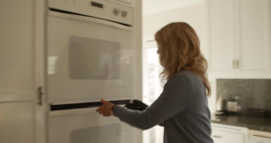 Woman wearing oven mitt removes cake pans from oven setting them on counter as husband watches