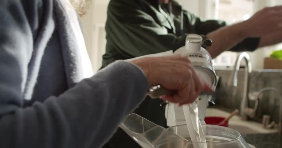 A woman uses a knife to slice butter and place the butter into the mixing bowl of an electric mixer in a home kitchen during the day