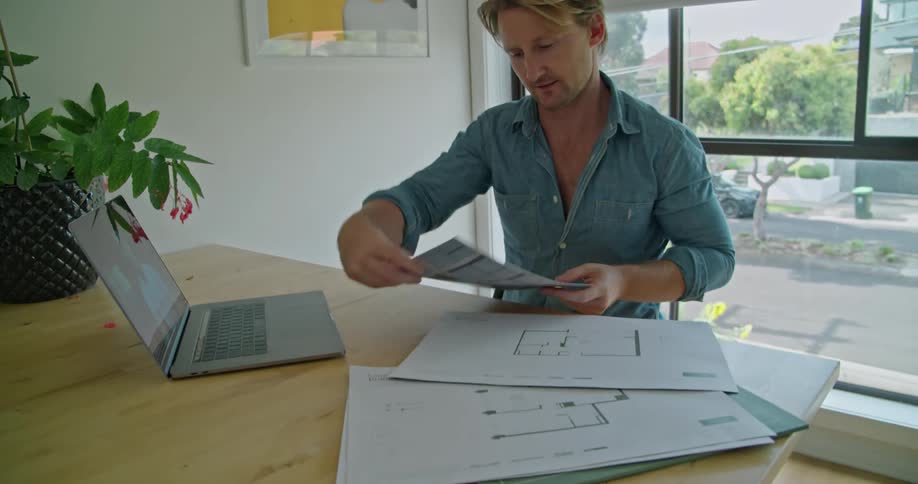 Man discusses diagrams on paper with another via video call on laptop