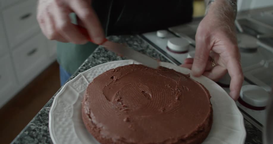 A man turns a plate as he frosts a chocolate cake