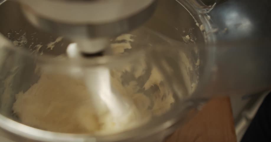Person stands next to standalone mixer mixing white frosting