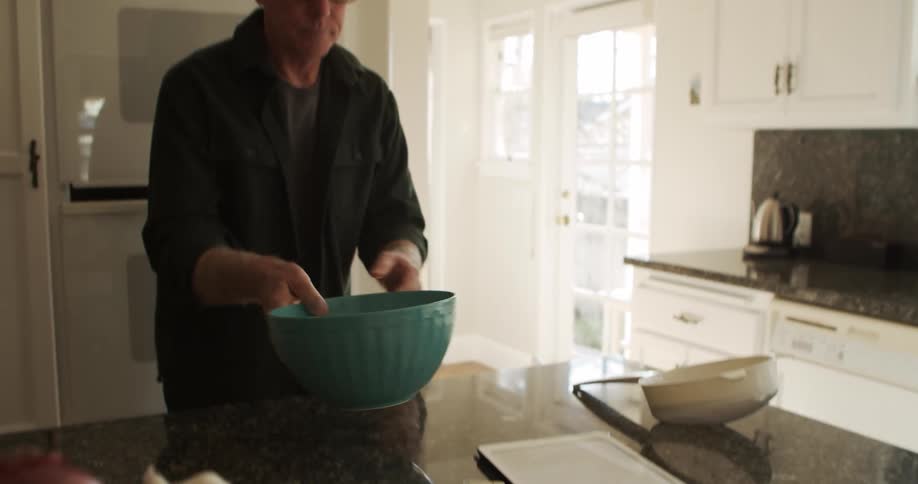 Man standing in kitchen pulls out bowl and places it on counter near bowl of fruit and vegetables
