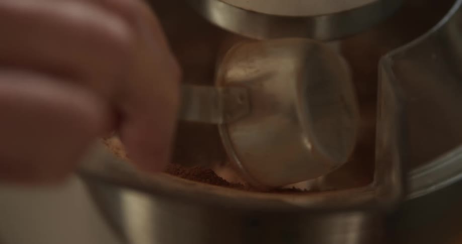 A baker adds cocoa powder to a spinning stand mixer