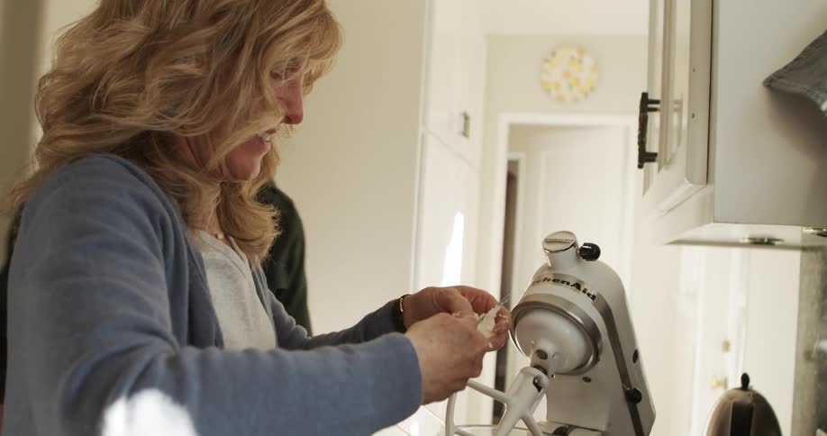 Woman laughs talking to man as she adds ingredients to standalone mixer