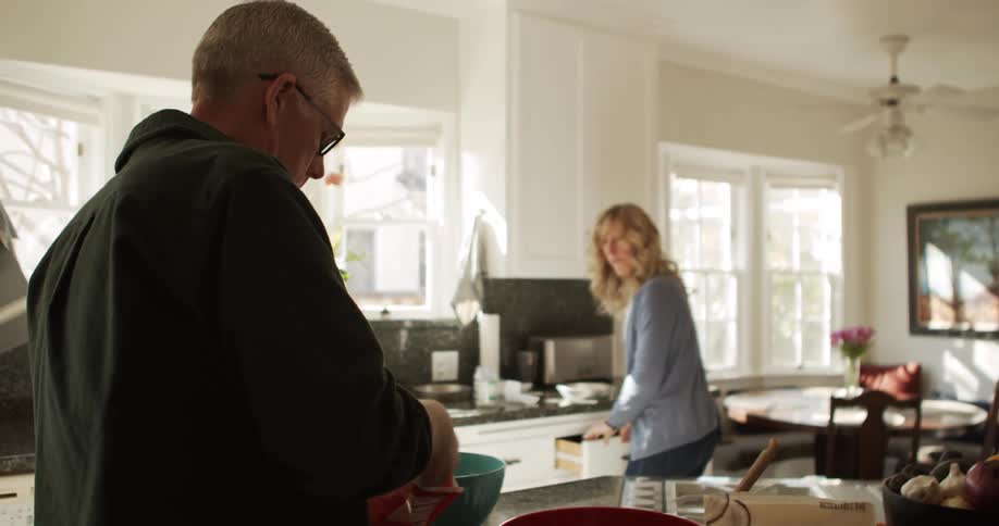 A man reaches into a plastic bag while preparing food in the kitchen with a woman