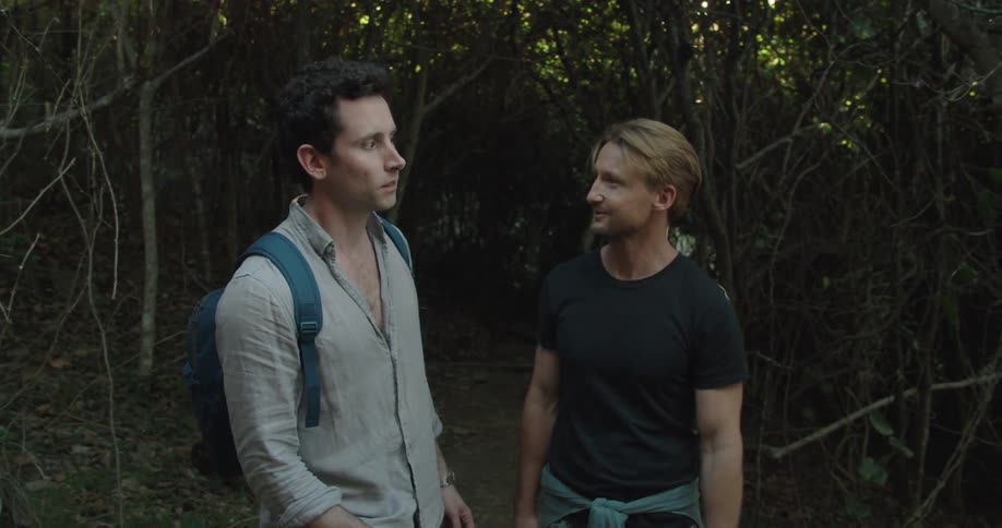 Blonde man with a black t shirt shows points out the forest to man with a backpack and a grey linen shirt