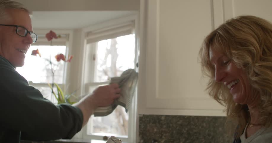A man and a woman in a kitchen with cabinets and windows in the background