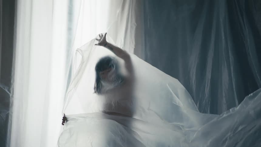 The silhouette of a woman with arms outstretched under a plastic sheet as it billows around her