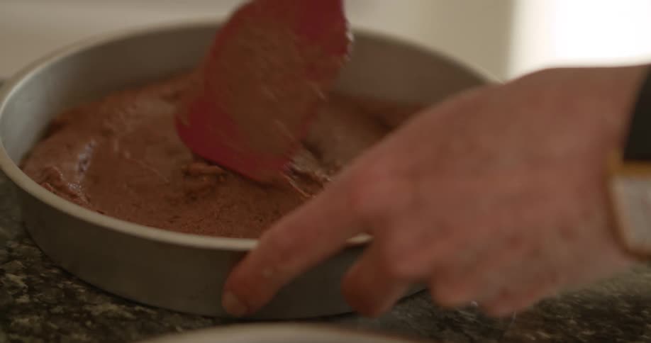 Hands hold a round baking pan and spread batter evenly with a spatula