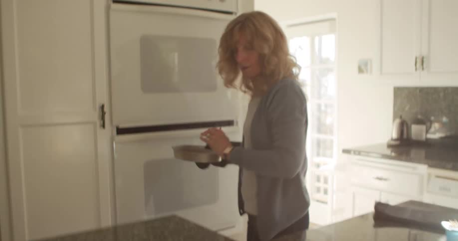 Blonde woman takes out cake out of oven in the kitchen