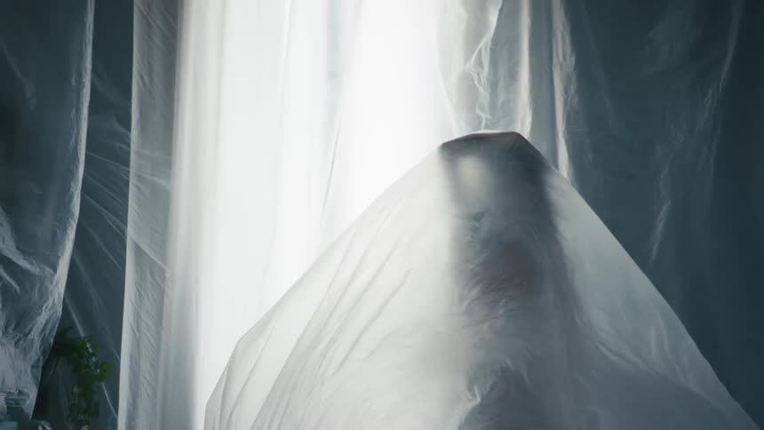 A woman extends her arms while standing beneath a thin sheet that covers the entire room
