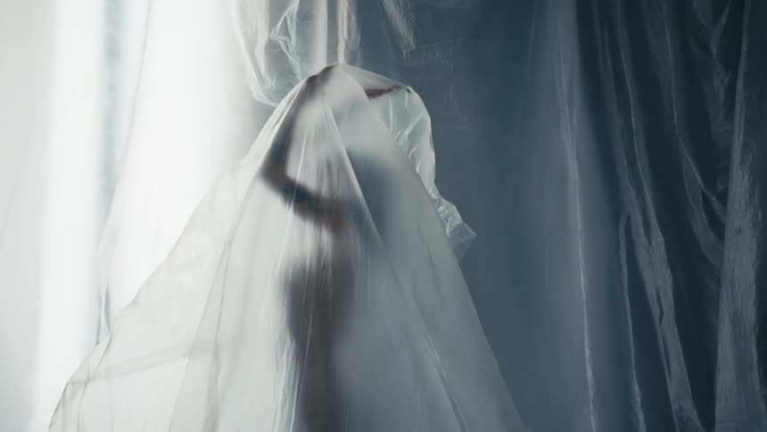 A woman holds her arms above her head while covered by a large sheer sheet of fabric