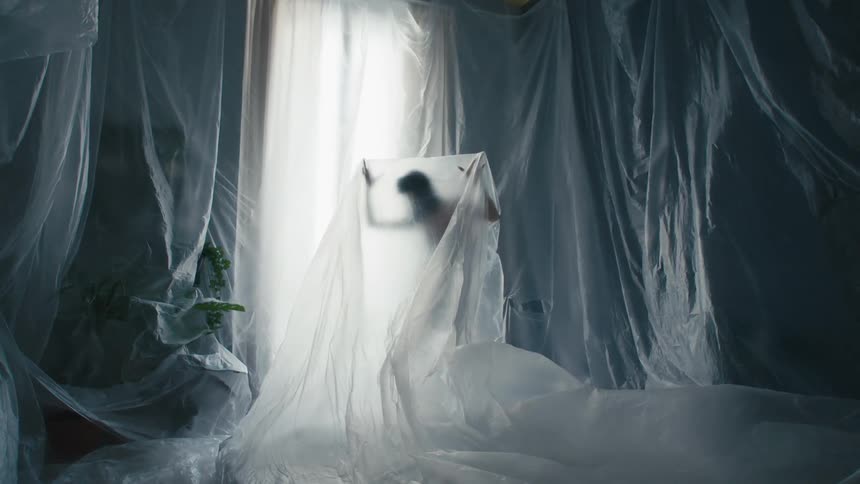 A woman poses under a clear tarp as wind blows through
