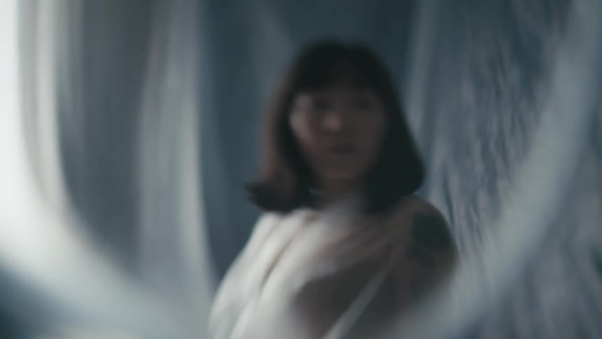 A woman wrap in a sheer sheet is surrounded by flowing fabric in this surreal environment