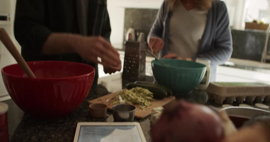 A man and a woman in a kitchen preparing food with bowls and a tablet on the counter