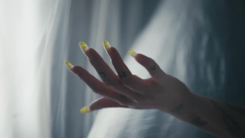 A woman with tattoos and painted nails extends and opens in a room covered in fabric