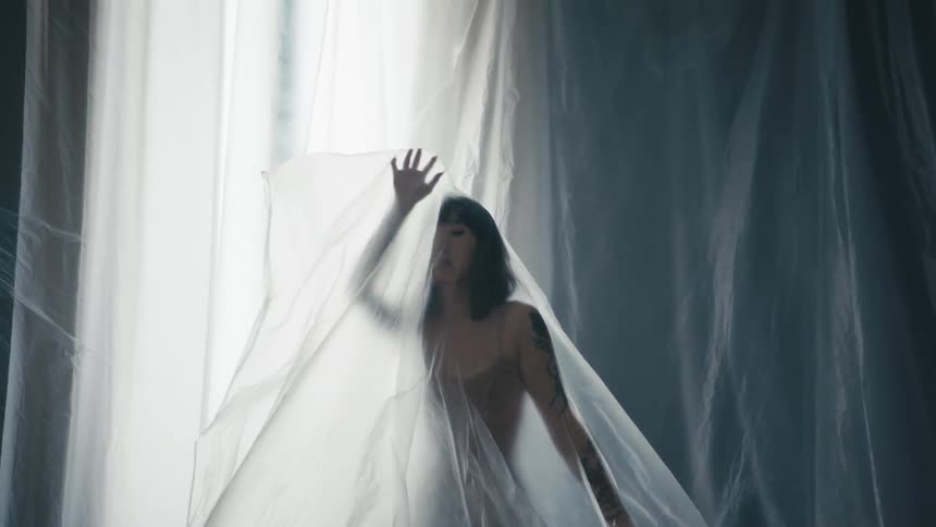 A woman waves her arms while standing beneath a large sheer piece of fabric